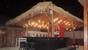 Un área de bar al aire libre con techo de paja, mostrador negro y asientos.