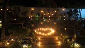 A nighttime outdoor area with a circular arrangement of lights on a wet surface, palm trees, and a building in the background.