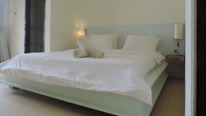 Una cama bien hecha con sábanas blancas, una lámpara de pared y una mesita de noche pequeña con lámpara.