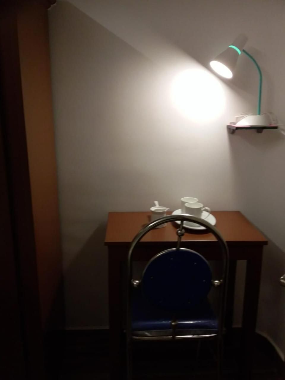 A small room with a wooden table, a blue chair, and a wall-mounted lamp.