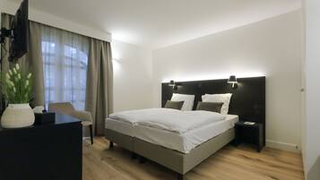 A modern bedroom with a large bed, a desk with a flat-screen TV, and a chair.
