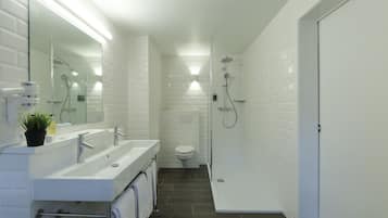 A modern bathroom with white subway tiles, a glass-enclosed shower, a white sink with a mirror, and a toilet.