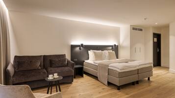 A modern hotel room with a sofa, a small table with a cup, a bed with a headboard, and a wardrobe.