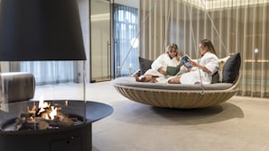 Un área de estar moderna con un sofá circular de mimbre, una mesa redonda negra con chimenea y una lámpara colgante grande.