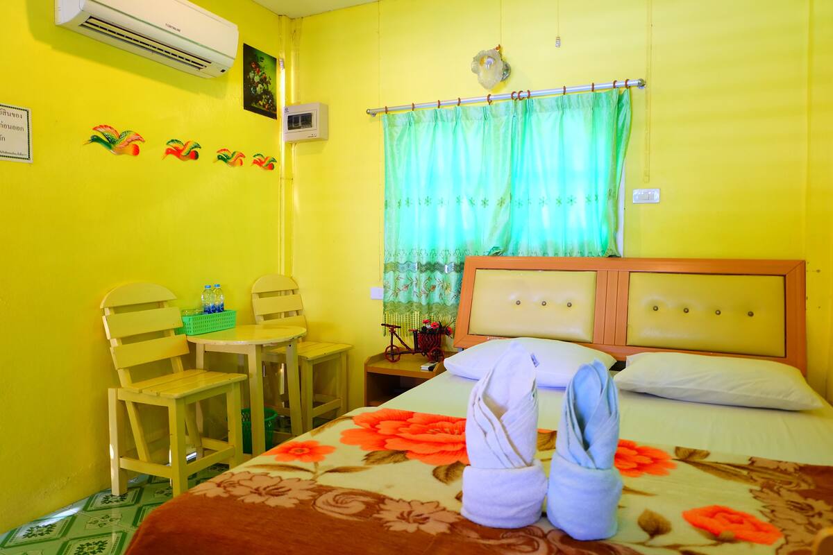 A room with a bed, a chair, a small table, and a wall-mounted air conditioner.