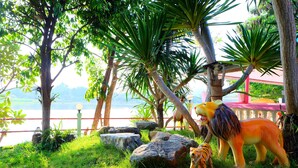 A tropical garden with a statue of a lion and a tiger, surrounded by rocks and palm trees. - Khunya Resort Riverkwai (Kanchanaburi)