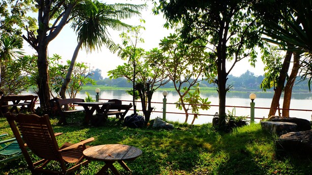 A lakeside patio with wooden furniture, a view of the lake, and surrounding greenery. - Khunya Resort Riverkwai (Kanchanaburi)
