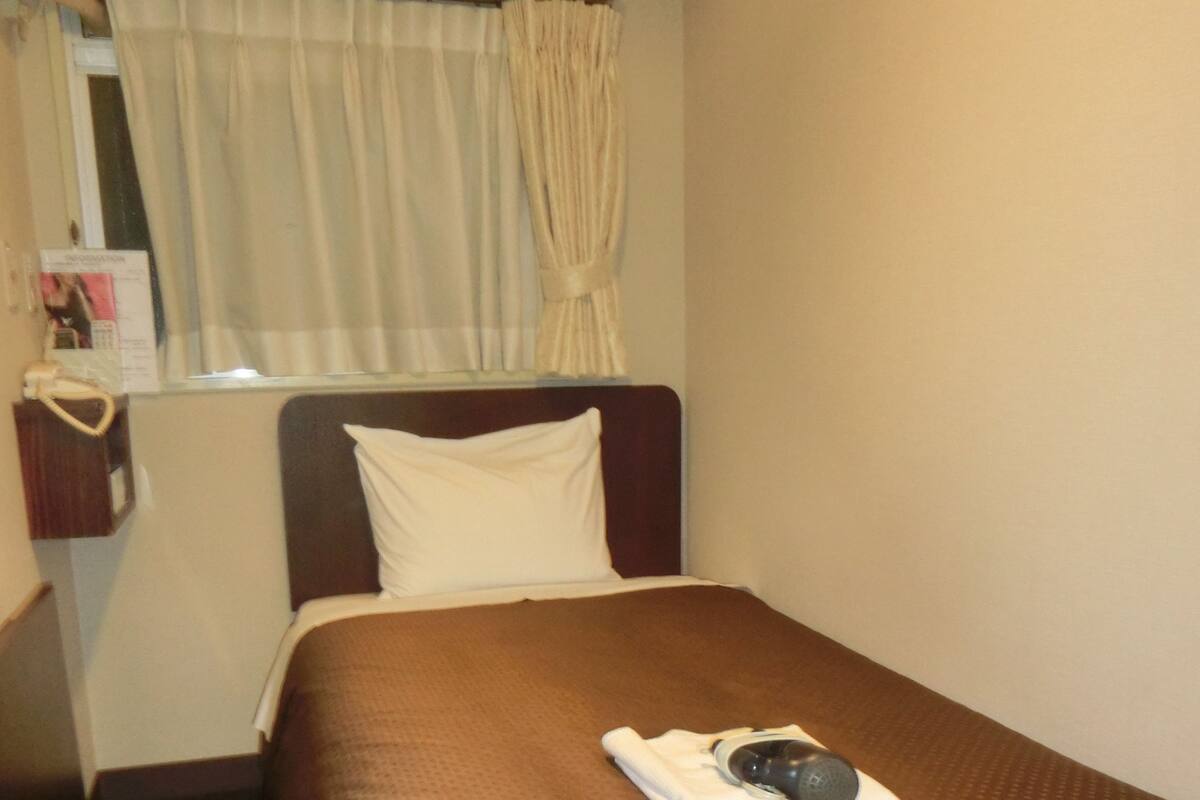 A hotel room with a single bed, a bedside table with a lamp, and a window with curtains.