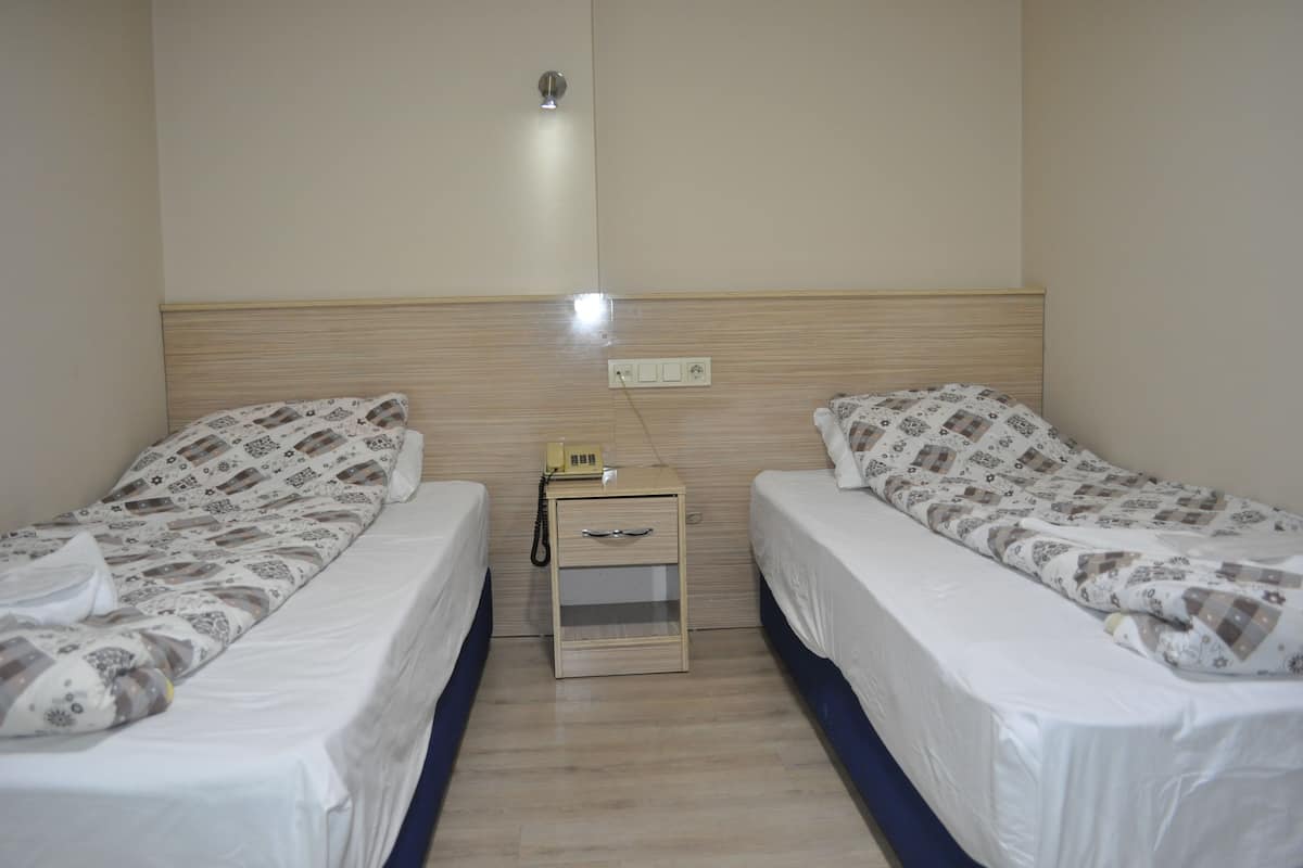 A twin room with two beds, a bedside table with a telephone, and a wall socket.