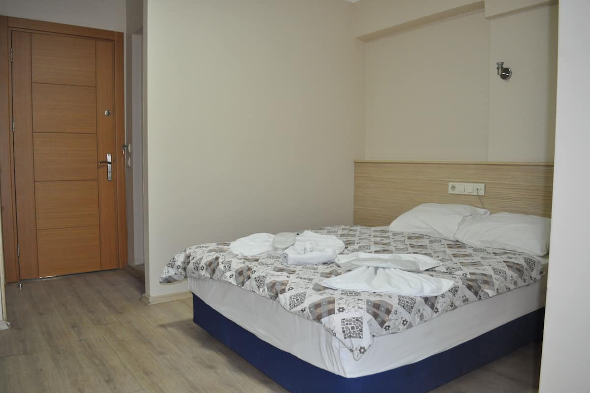 A bedroom with a wooden door, a bed with patterned bedding, and a plain wall with a light switch.