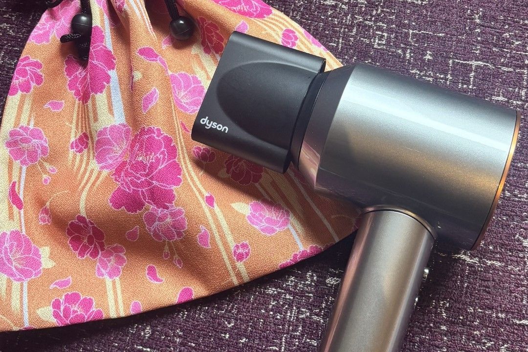 A Dyson hair dryer placed on a patterned fabric surface.