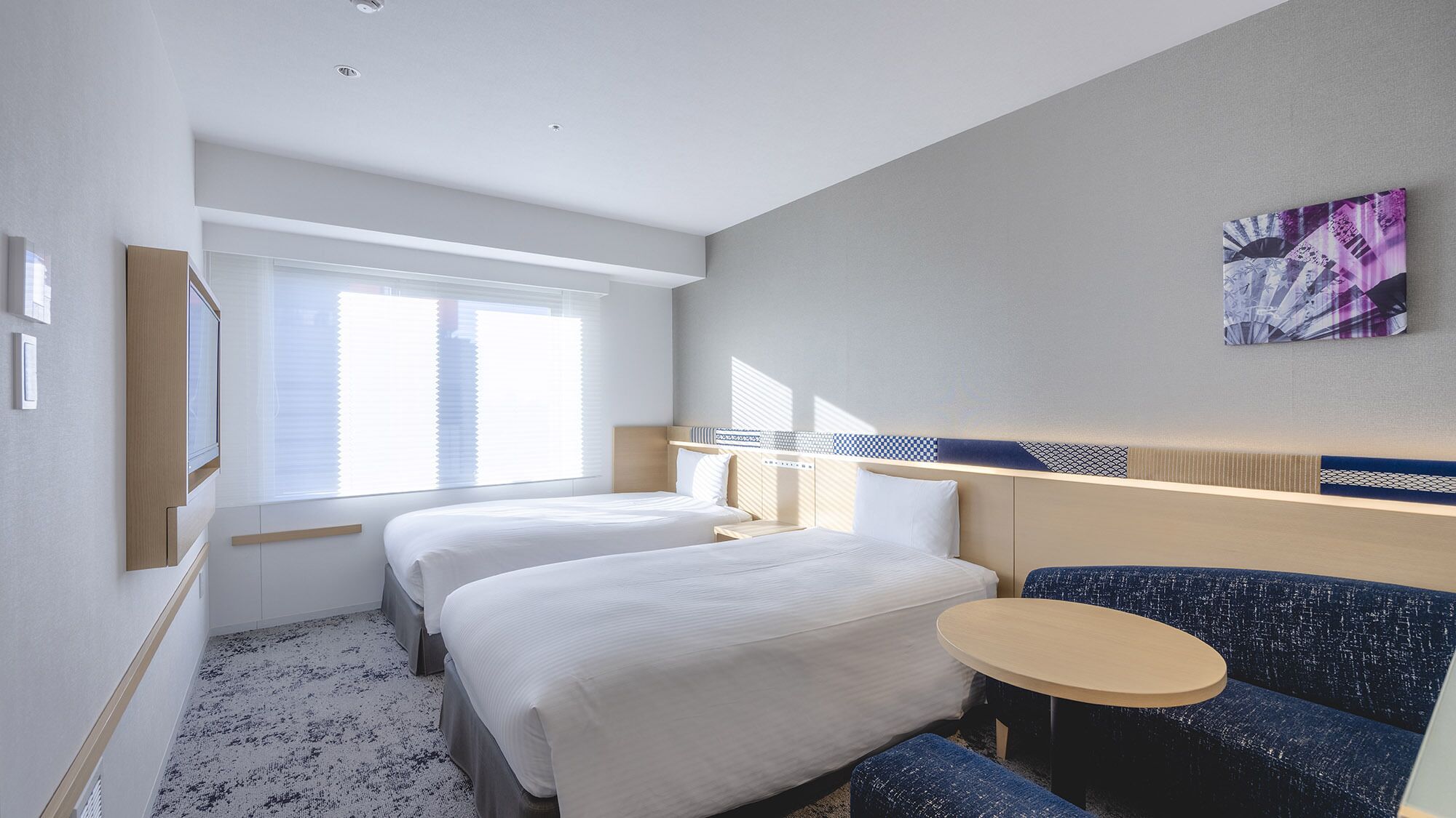 A hotel room with two beds, a small round table, and a blue sofa.