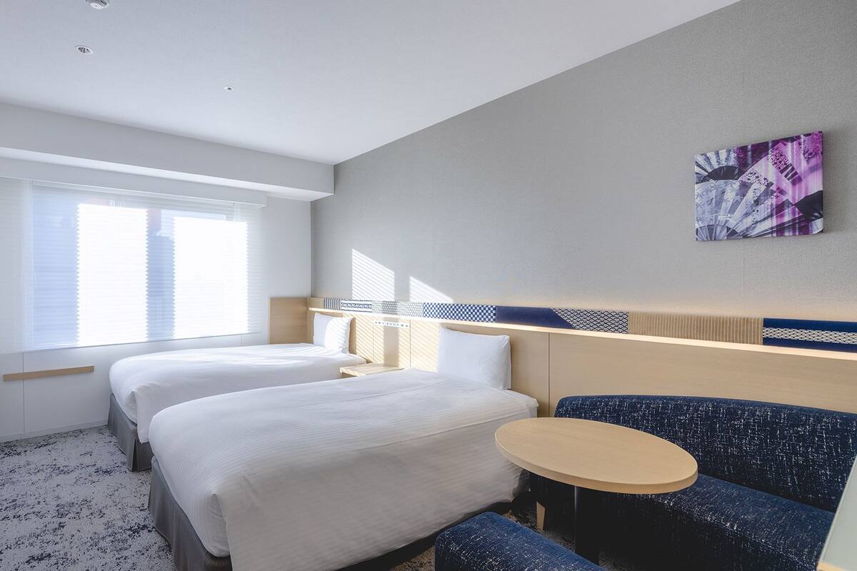 Une chambre d’hôtel avec deux lits, une petite table ronde et un canapé bleu.