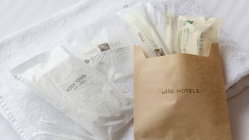 A set of toiletries including a body towel, a shower cap, and a hairbrush, all packaged in a brown paper bag with 'WHG HOTELS' branding.