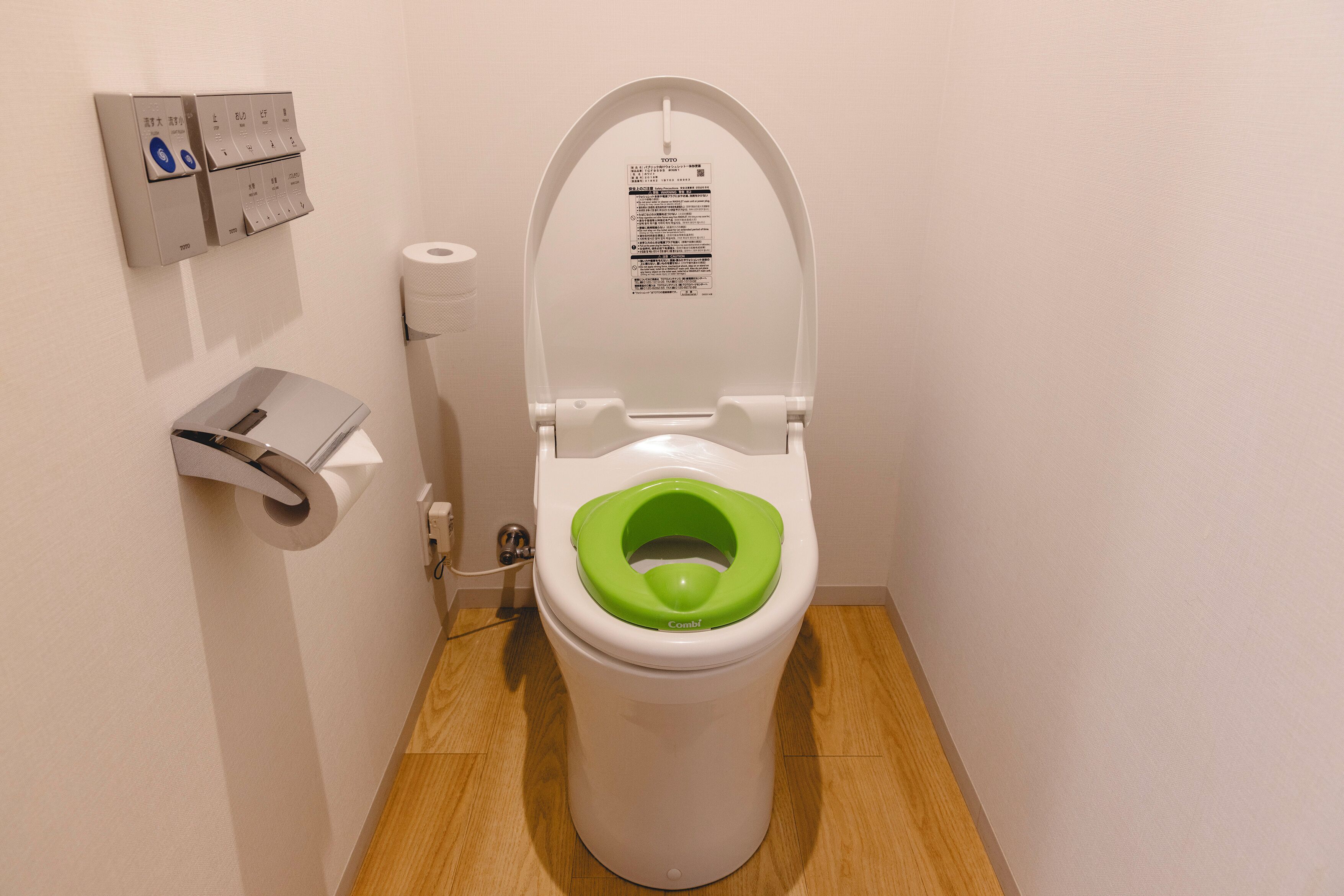 A toilet with a green seat cover, a toilet paper holder, and a flush button.