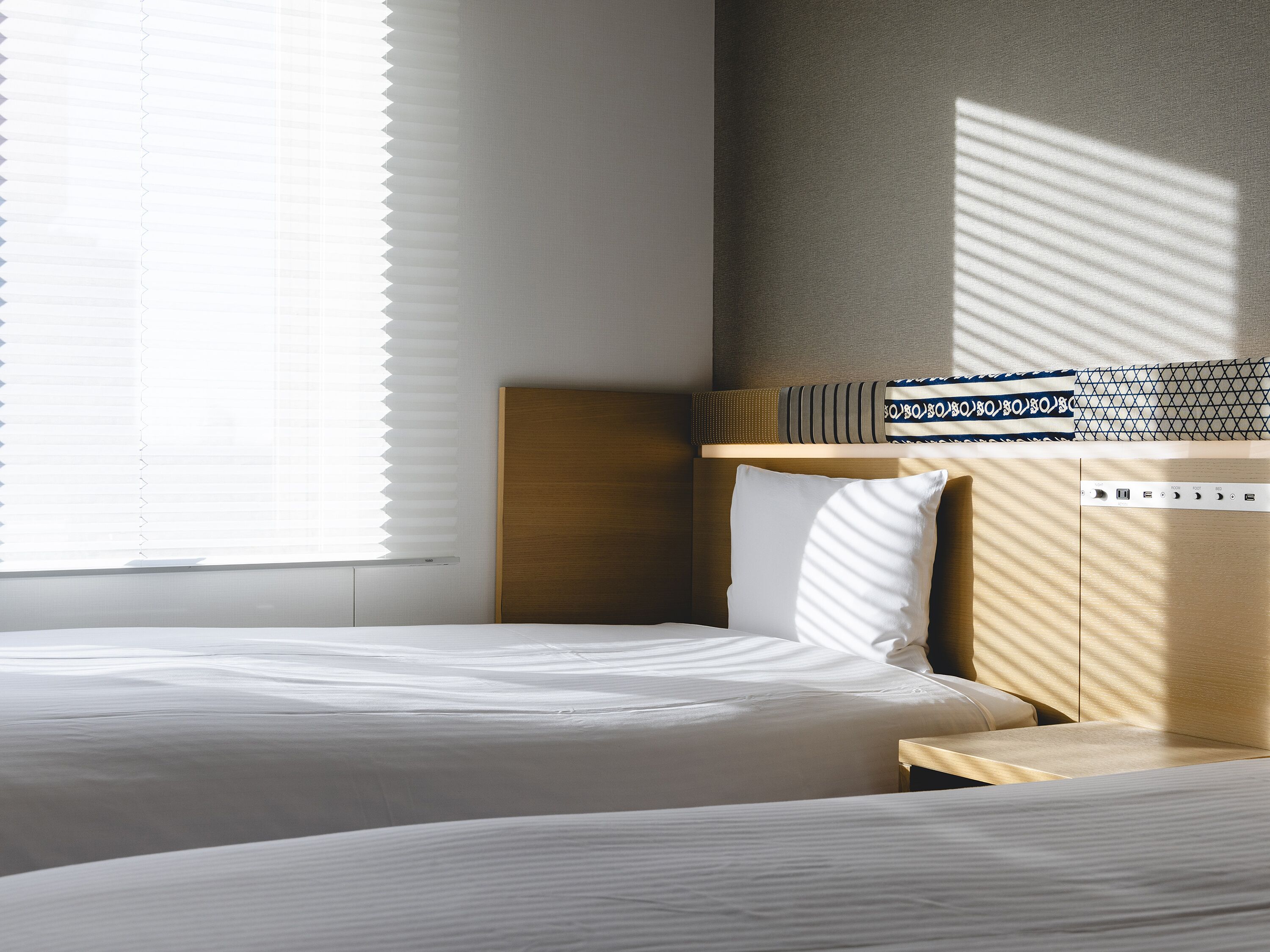 Une chambre d’hôtel avec deux lits, une tête de lit en bois, une table de chevet et un panneau de commande fixé au mur.