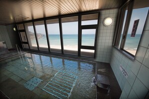 An indoor swimming pool with clear views of the beach through large windows. - Kokuminsyukusya Senjoen (Hamada)