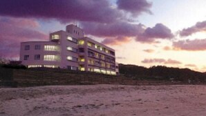 Un edificio de varios pisos con techo plano, situado cerca de una zona arenosa.