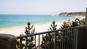 Vista a la playa desde un balcón con barandilla, cielo despejado y mar tranquilo.