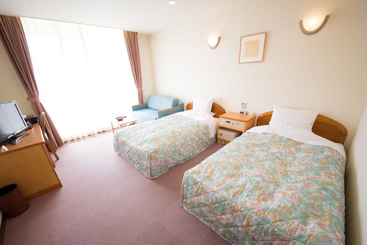 Ein Hotelzimmer mit zwei Betten, einem Schreibtisch, einem Stuhl und einem Fernseher.