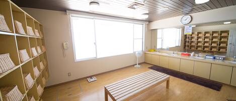 Ein Zimmer mit Holzboden, einer Bank, Weidenkörben auf Regalen, einem Fenster, einer Uhr und einer Theke mit Waschbecken.