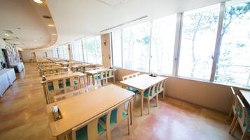 A spacious dining area with multiple tables and chairs, large windows providing natural light, and a clean, modern interior design.