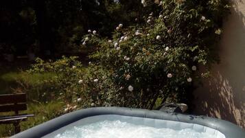 Relax in a serene garden setting with a hot tub surrounded by lush greenery and a wooden bench for unwinding.