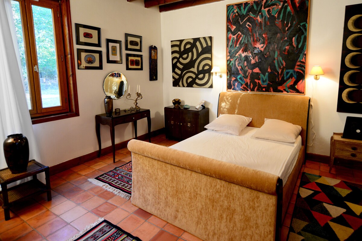 A bedroom with a bed, a dresser, a nightstand, a mirror, and artwork on the walls.