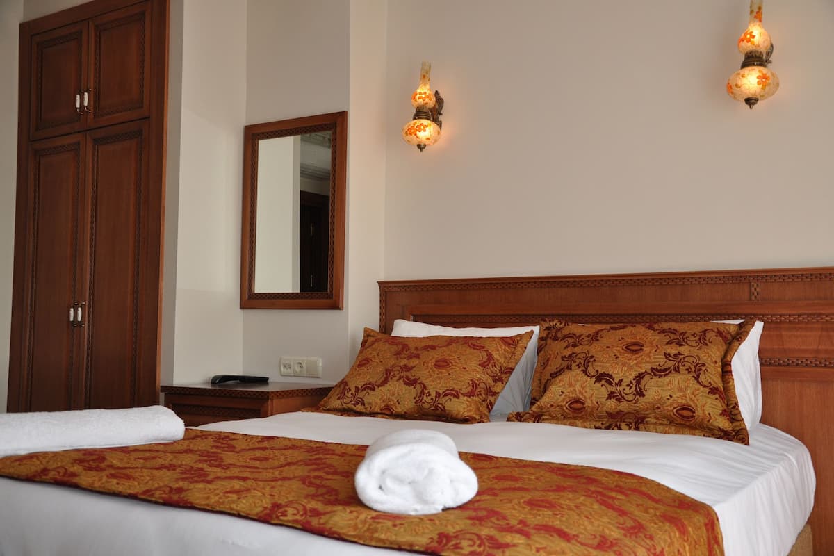A hotel room with a large bed, wooden headboard, two wall sconces, a mirror, and a wardrobe.