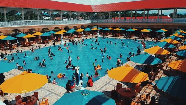 Una gran piscina al aire libre con múltiples sombrillas y sillas de descanso.