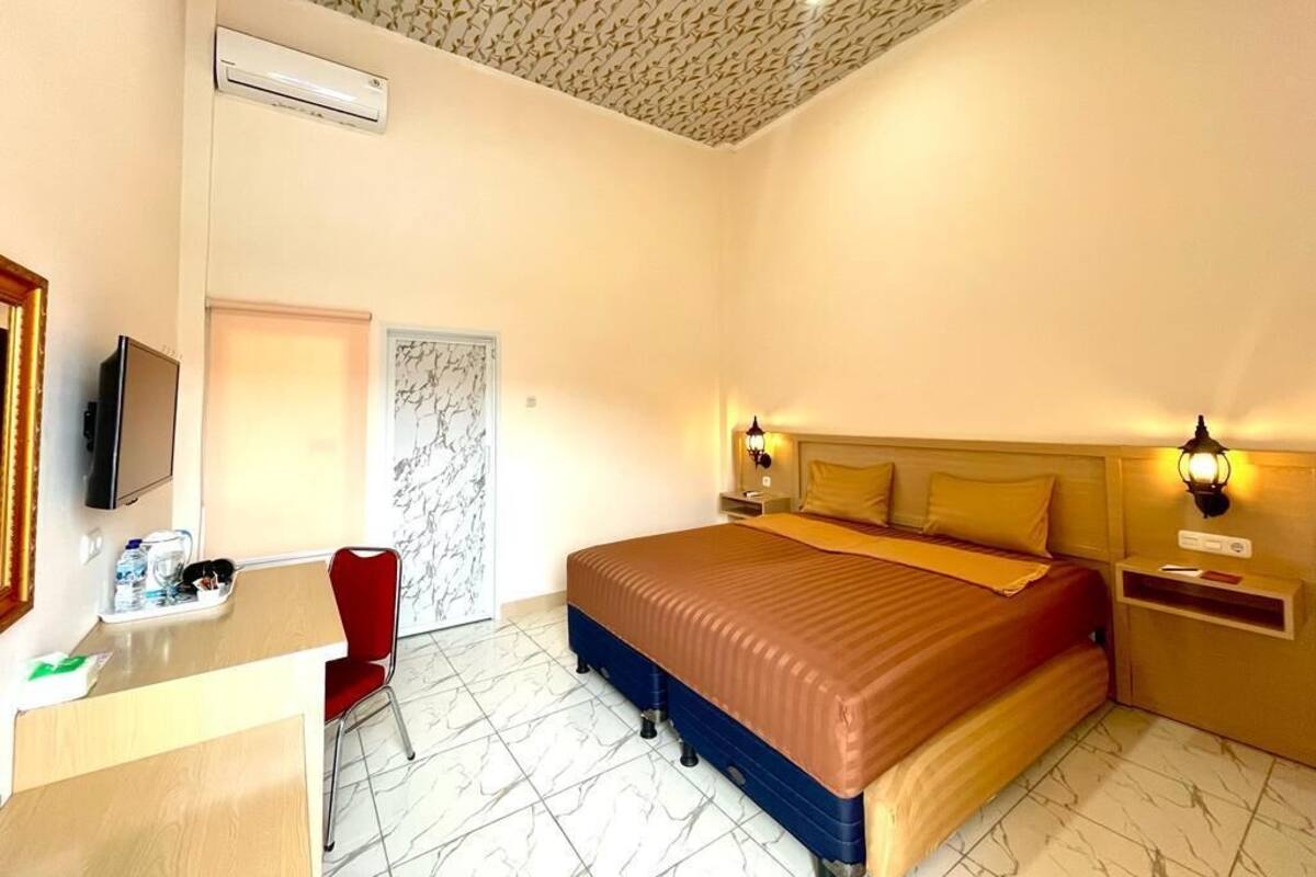 A hotel room with a bed, bedside tables, a desk with a chair, and a television.