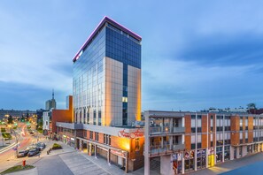 Un hotel moderno con fachada de vidrio, una entrada destacada y un estacionamiento con automóviles.