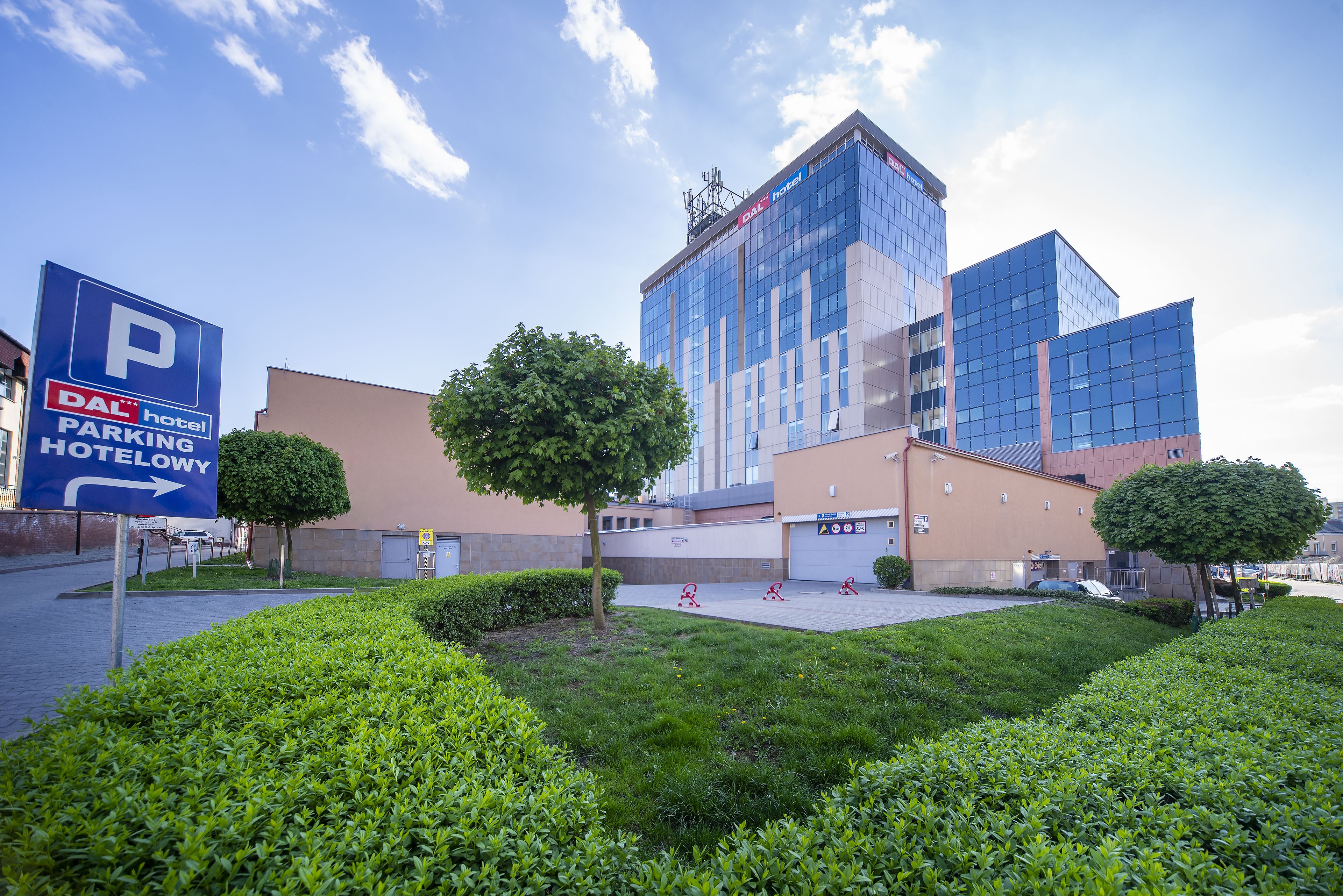 A modern hotel with a parking sign, well-maintained lawns, and a clear sky.