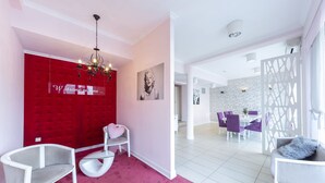A modern living room with a red accent wall, a chandelier, and a dining area with purple chairs. - Hotel Dal Kielce (Kielce)