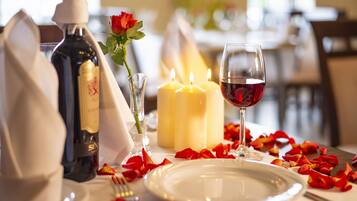 A table set for two with candles, a bottle of wine, a glass of wine, rose petals, and a rose.