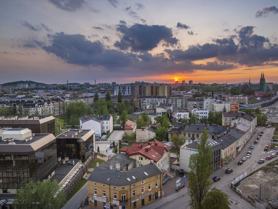 Une vue urbaine avec un coucher de soleil, des bâtiments et le clocher imposant d’une église.