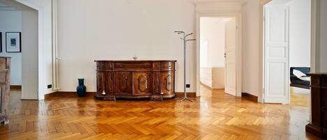 A spacious room with a wooden parquet floor, a large wooden cabinet, and a tall floor lamp.