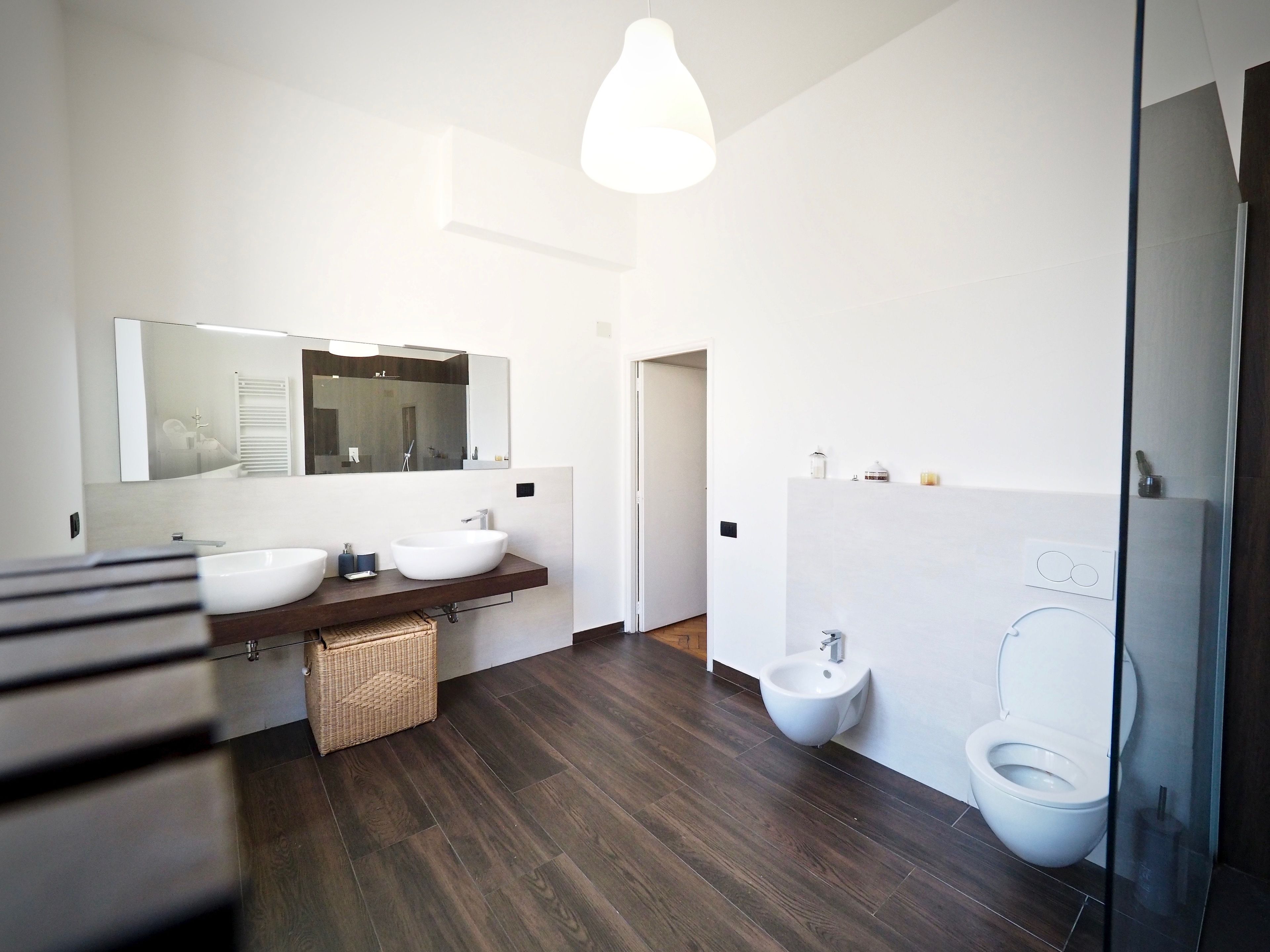 A modern bathroom with a large mirror, two sinks, a bidet, and a toilet.