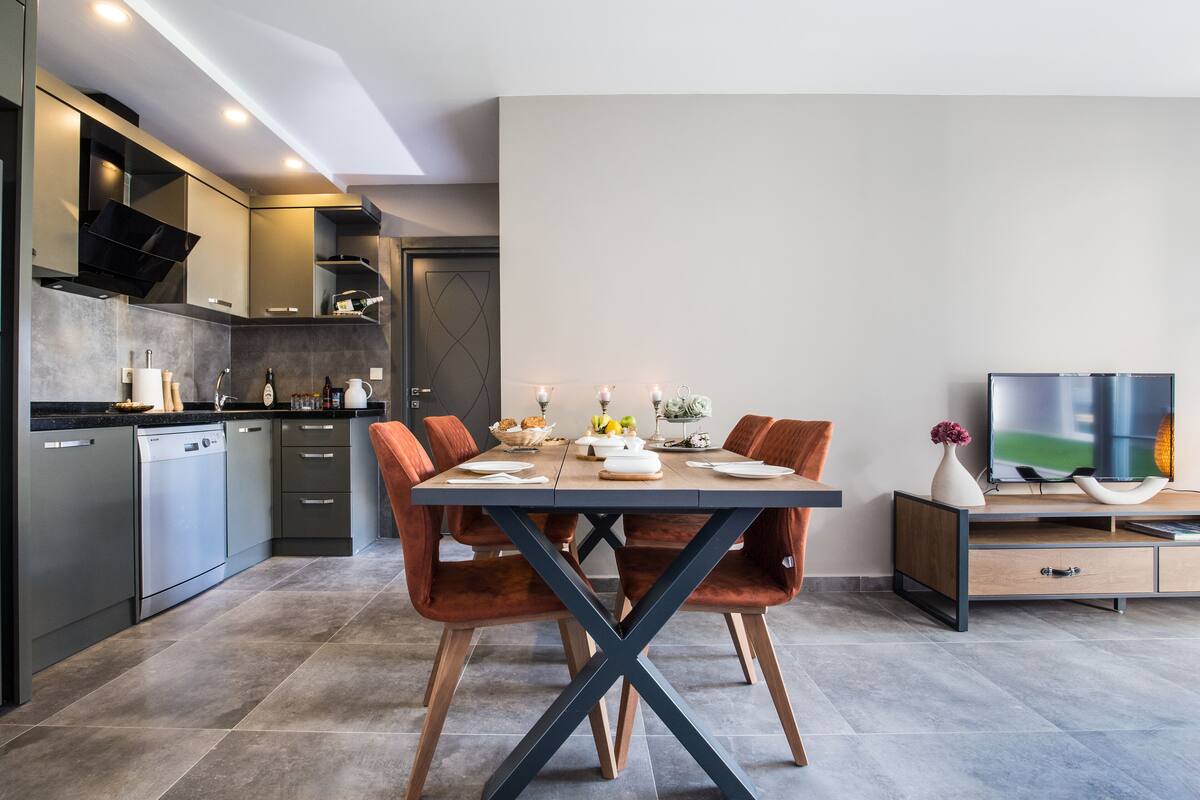 A modern kitchen with grey cabinetry, a dishwasher, and a dining area with a table set for four.