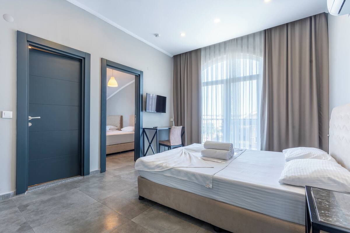 A modern hotel room with a large bed, a desk, a television, and a view of the outdoors.