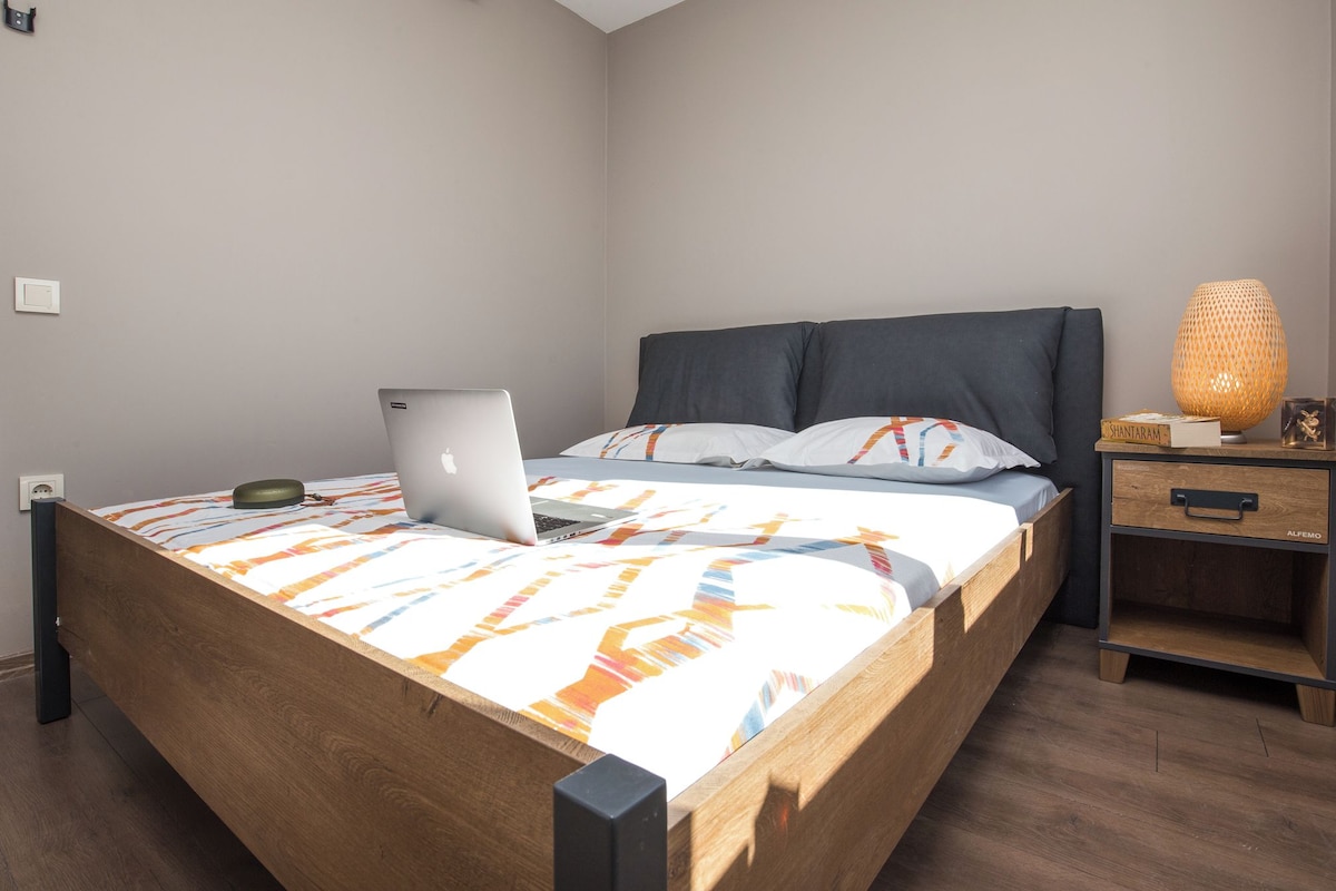 A neatly made bed with a laptop, a bedside lamp, and a nightstand with a drawer.
