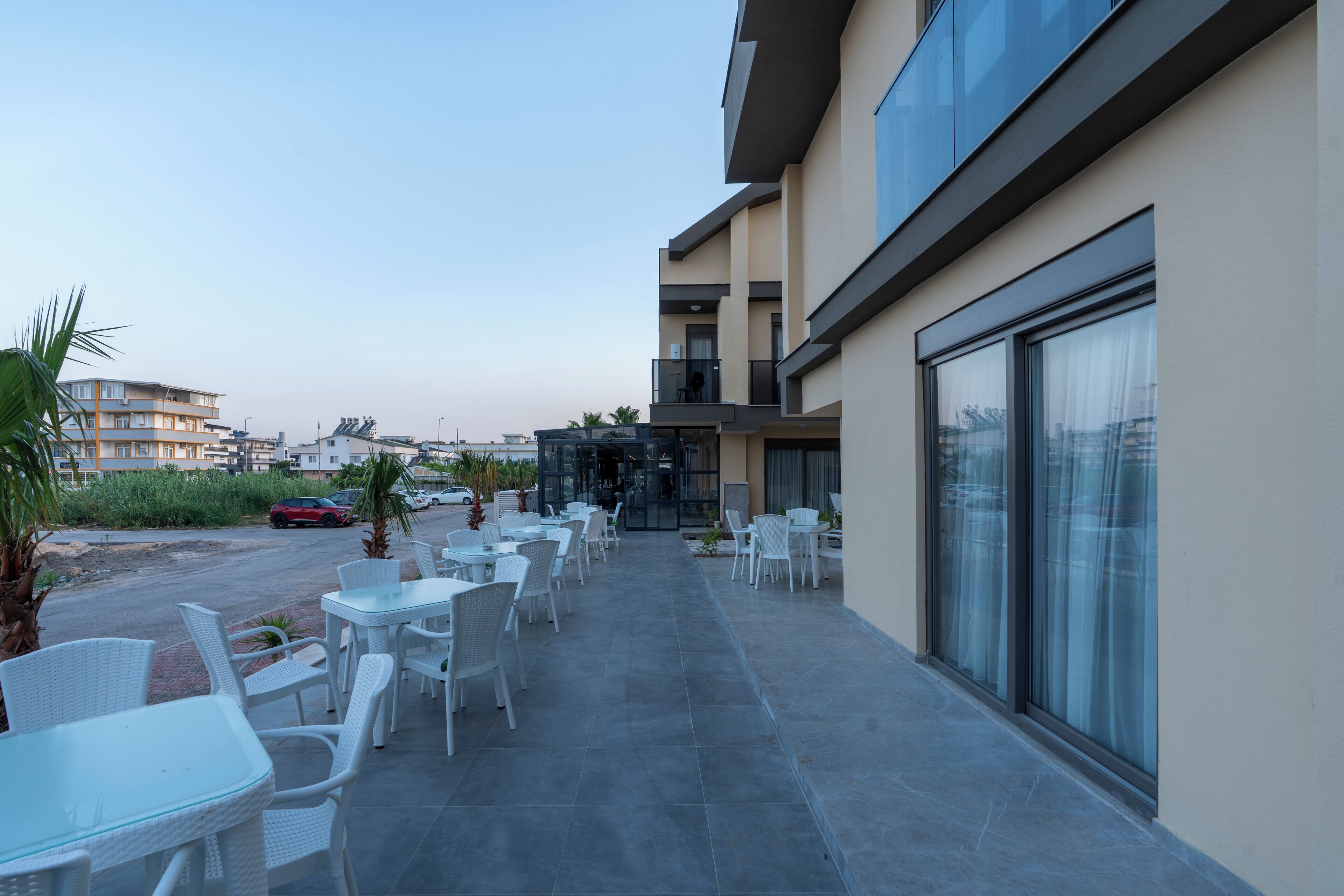 Une terrasse extérieure moderne, avec des tables et des chaises en osier blanc, un ciel dégagé et une vue sur les bâtiments environnants.