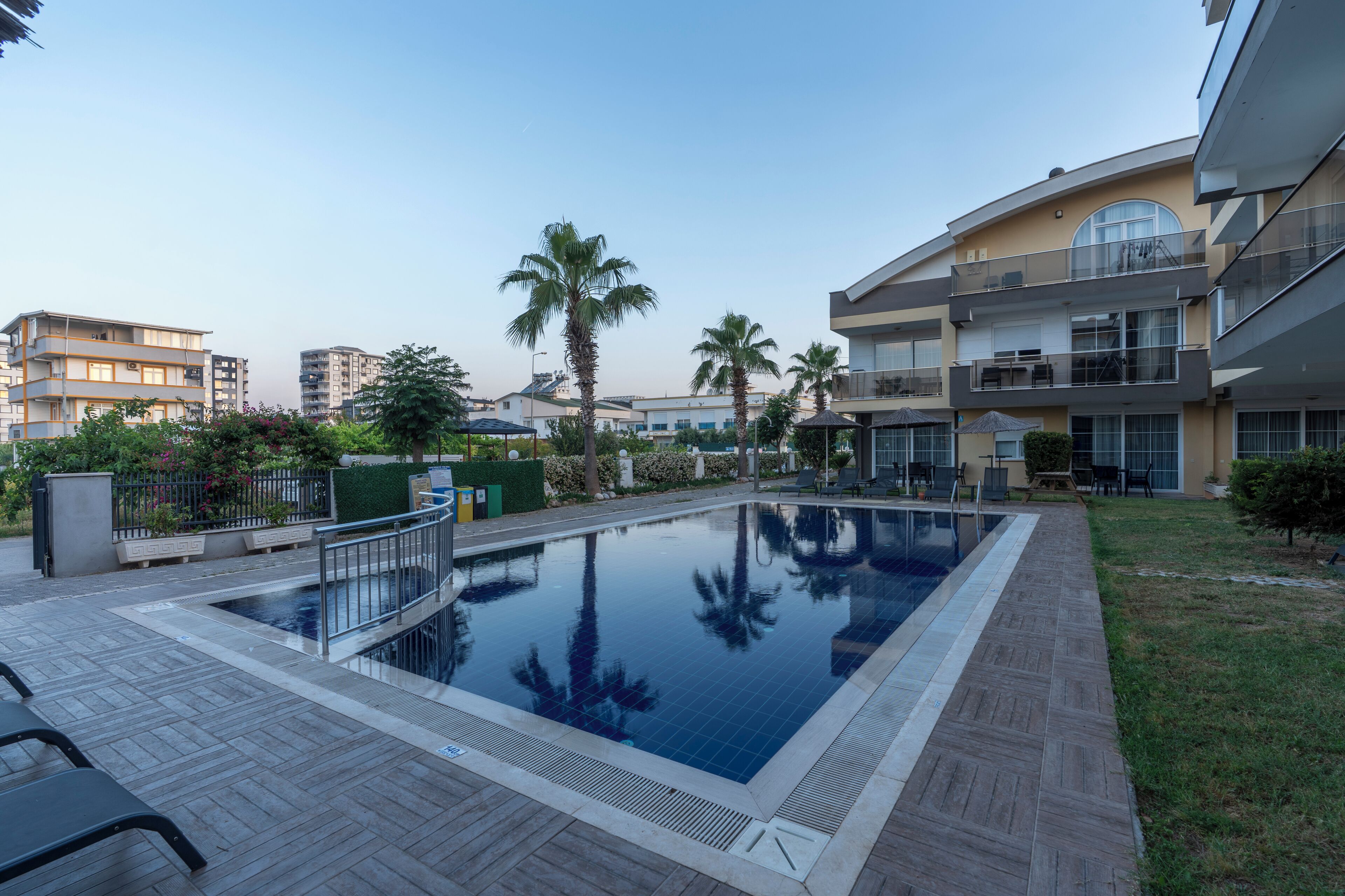 A swimming pool with a tiled deck, surrounded by palm trees and modern buildings.