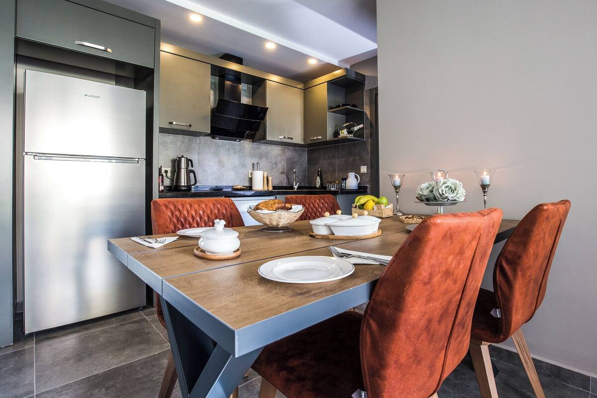 A modern kitchen with a built-in refrigerator, a dining table with chairs, and a kitchen counter with various appliances and items.