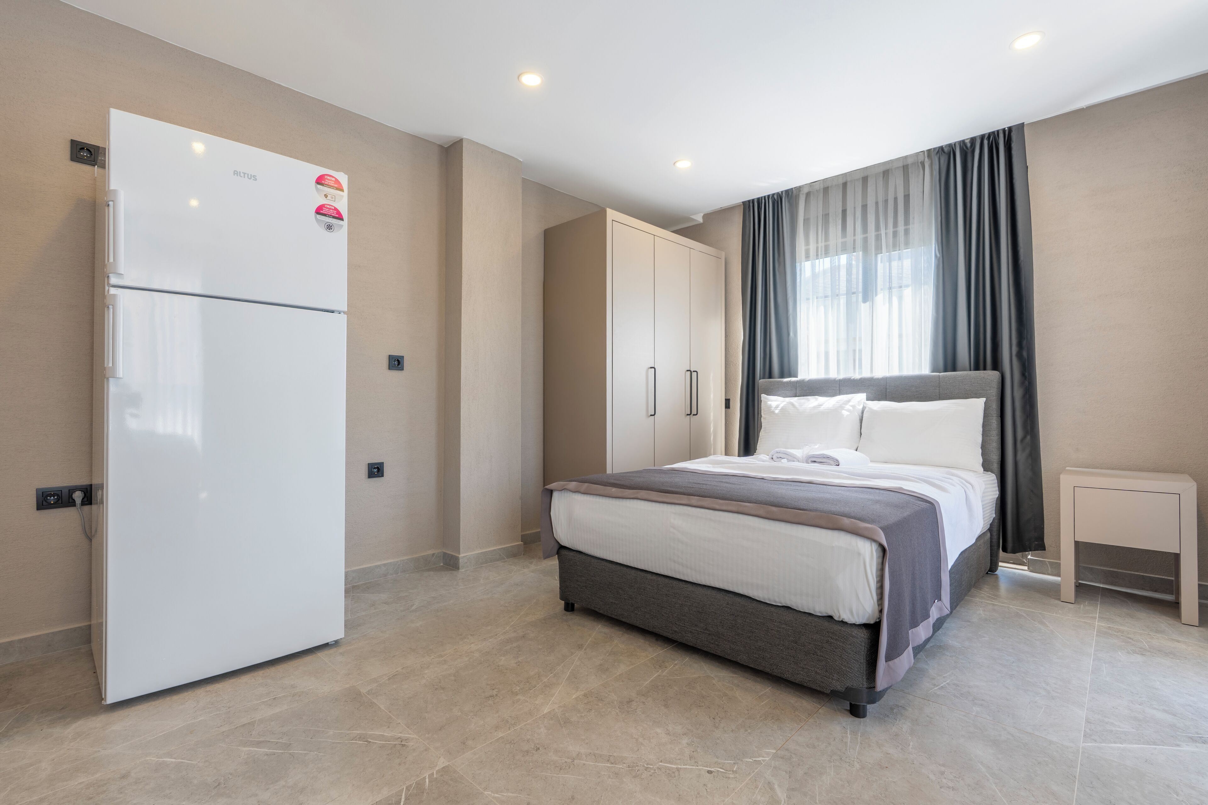 A modern bedroom with a bed, a wardrobe, a small bedside table, and a built-in refrigerator.