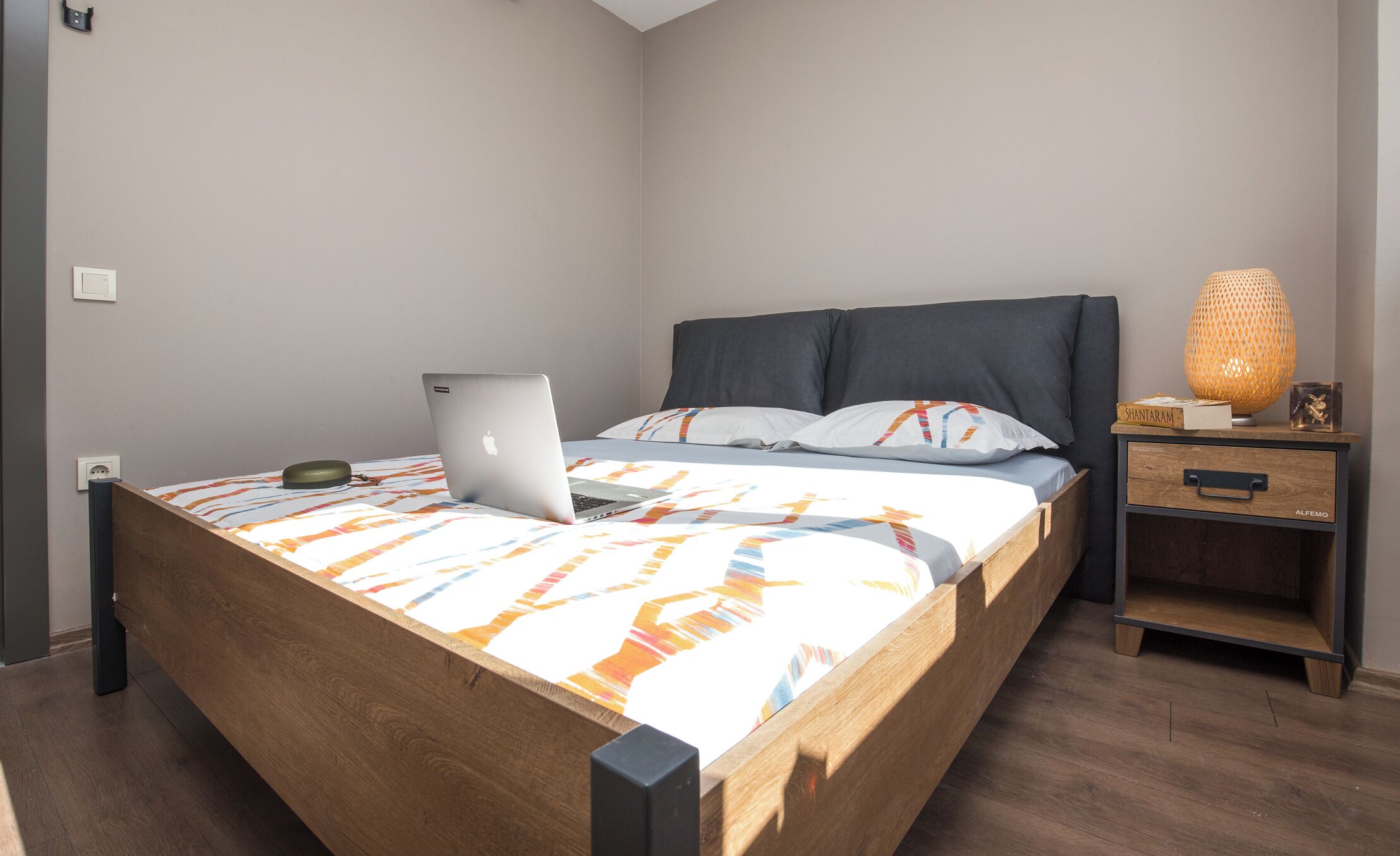 A bed with a laptop, a bedside lamp, and a nightstand with a drawer.