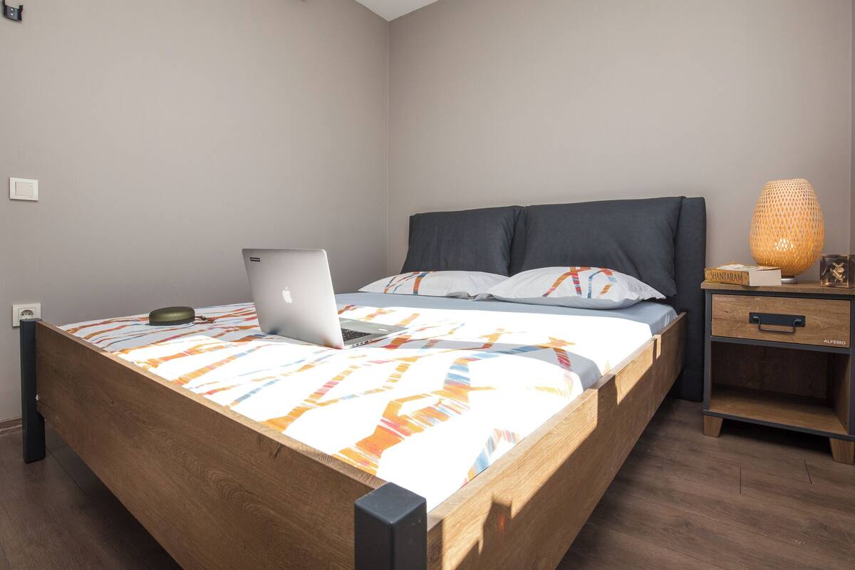 A neatly made bed with a laptop, a bedside lamp, and a nightstand with a drawer.