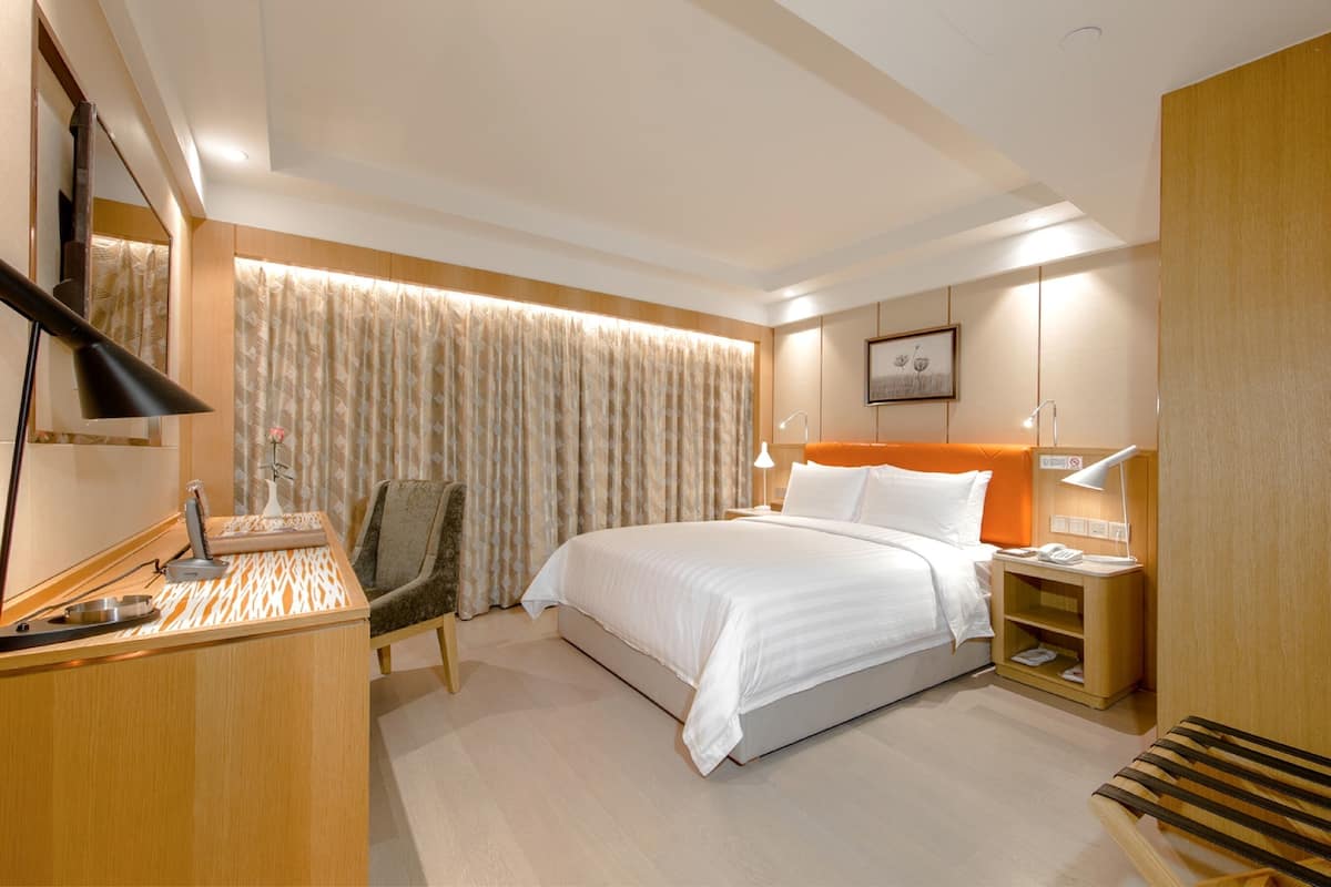 A hotel room with a bed, bedside table, lamp, chair, and a desk with a lamp.