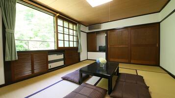 A traditional Japanese room with tatami flooring, a low table, cushions, a window with curtains, and a sliding door.