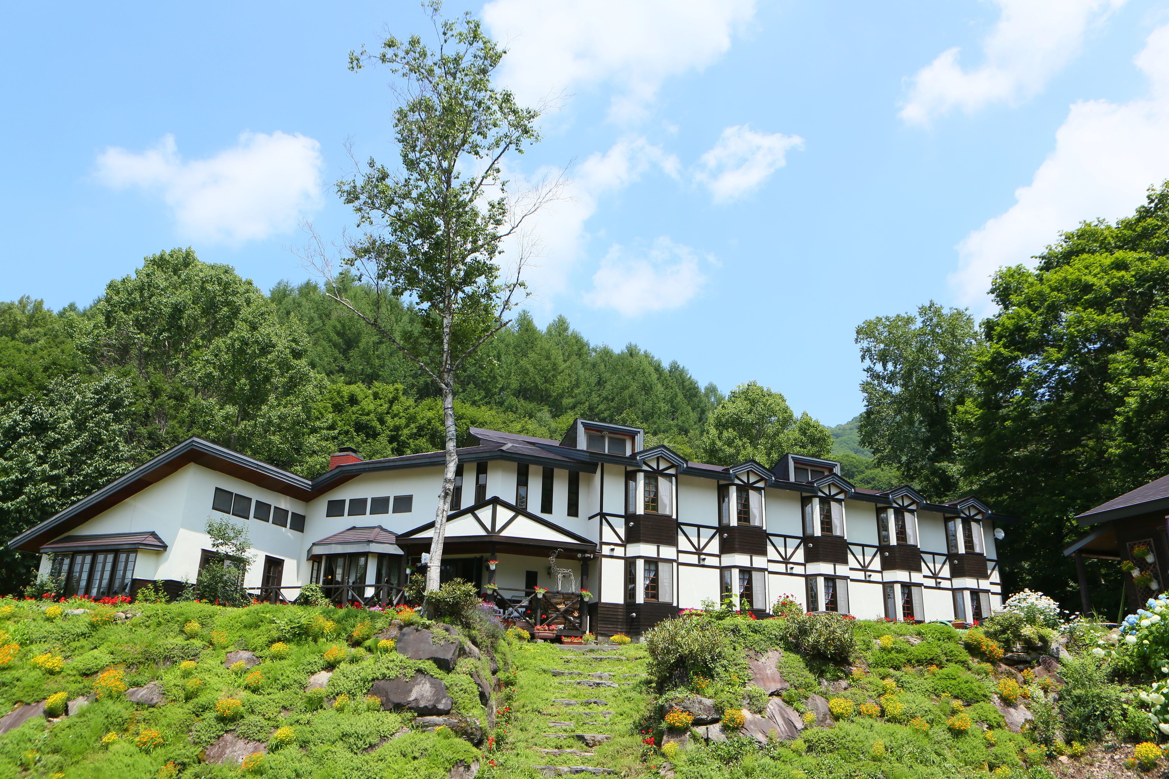 A large, multi-story building with a traditional architectural style, surrounded by lush greenery and a clear sky.